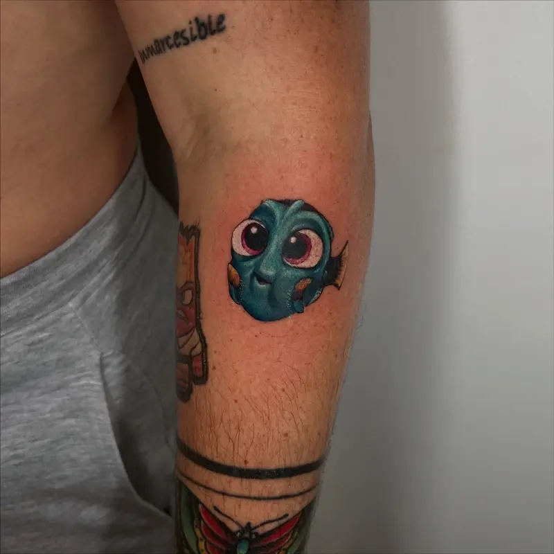 Tatuaje a color de pez azul estilo cartoon con ojos muy grandes y expresión tierna.