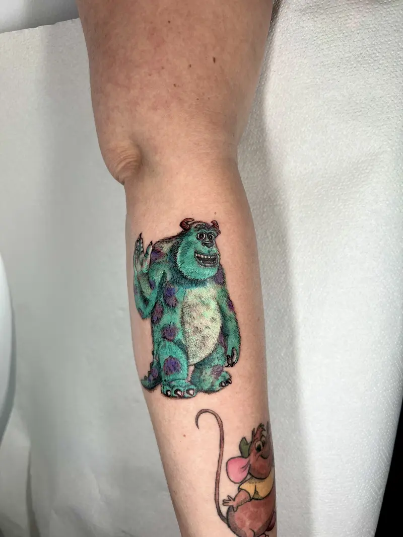 Tatuaje a color de monstruo peludo azul estilo animación saludando, con textura y volumen.