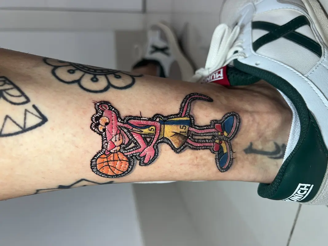 Personaje de pantera rosa jugando al baloncesto, estilo parche bordado con detalles de hilo.