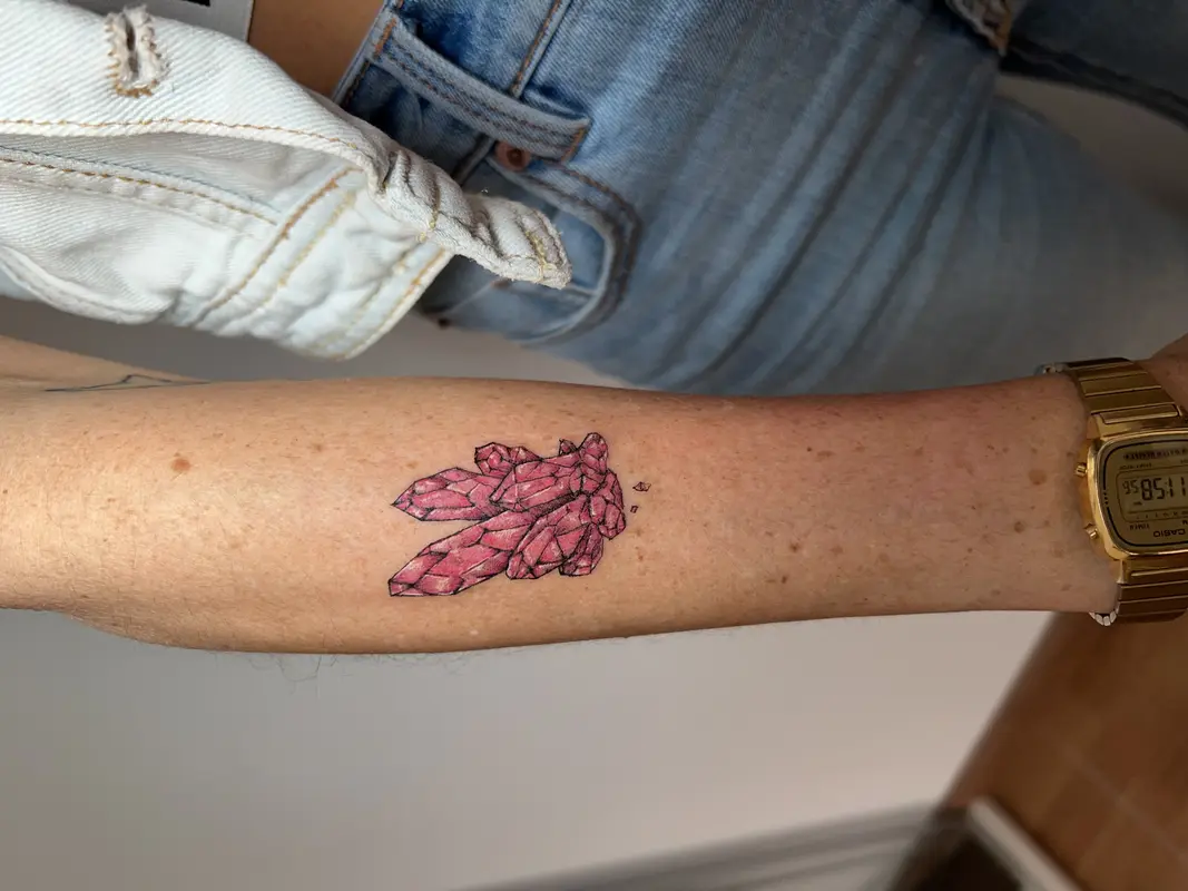 Cristal rosa facetado tipo mineral, estilo geométrico con líneas y pequeños fragmentos alrededor.