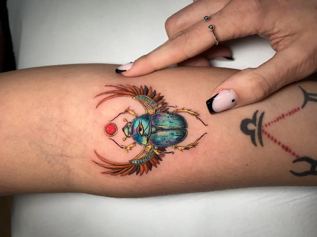 Escarabajo a color tipo amuleto con alas ornamentales y esfera roja, acabado brillante y detallado.