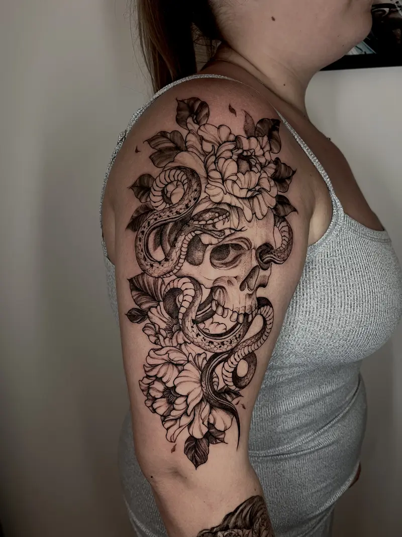 Tatuaje blackwork de calavera con serpiente y flores en brazo.