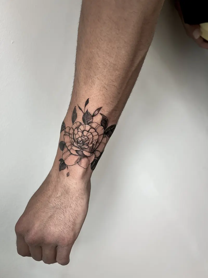 Rosa grande en black & grey con sombreado suave y hojas oscuras, colocada en el antebrazo.